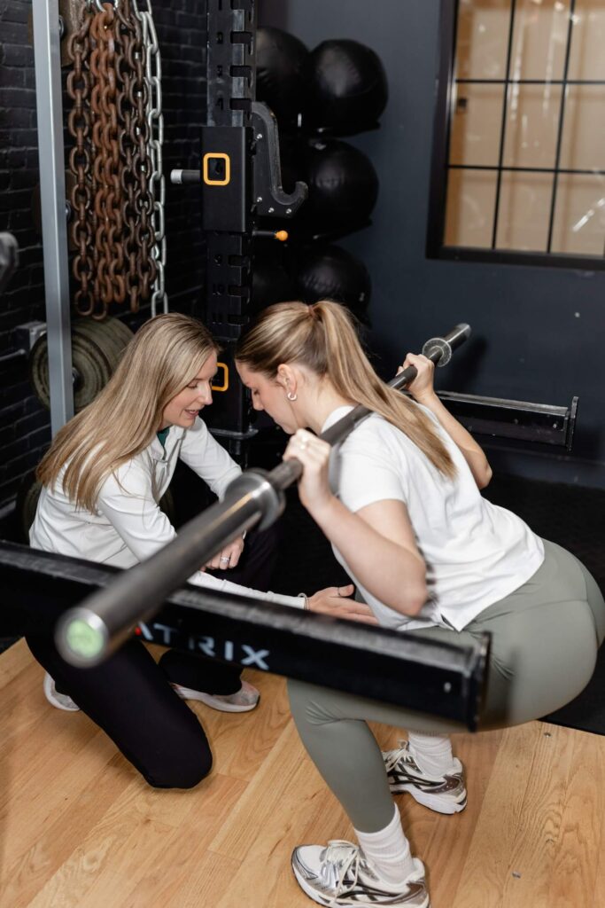 Dr Brooke helping a client squatting with a barbell